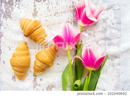 Three croissants and bright pink tulips on lace tablecloth 102040692