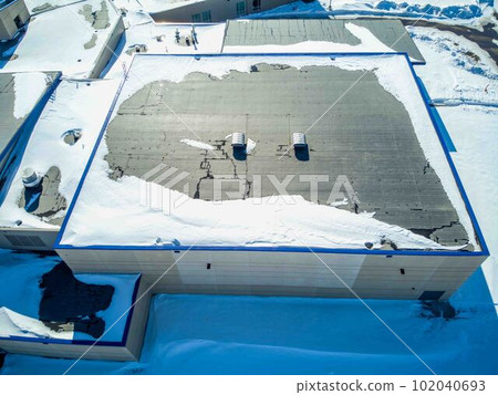 Elevated overhead drone view of a flat roofed building with snow load and ventilation units. Elevated overhead drone view of a flat roofed building with snow load and ventilation units. 102040693