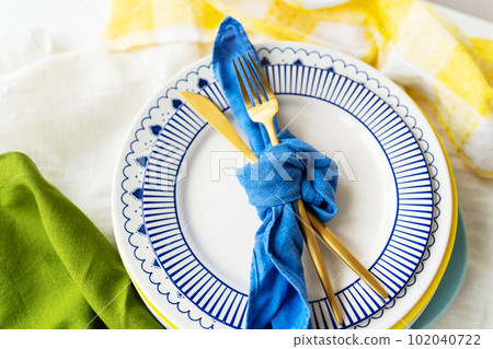 Serving design. Easter serving concept. Gold cutlery is tied with a blue napkin, on which the plates are on a green-yellow linen napkin. Minimalistic design. 102040722