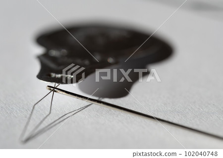 Sewing needle threader tool in use and a single black string.  102040748