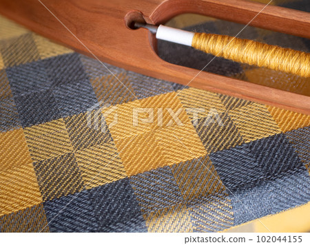 Woven checkered yellow and gray fabric on a hand loom with a wooden boat shuttle. Weaving detail Woven checkered yellow and gray fabric on a hand loom with a wooden boat shuttle. Weaving detail 102044155