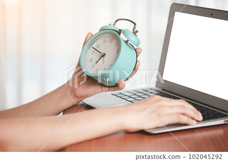 Woman's hand holding alarm clock to check the time 102045292