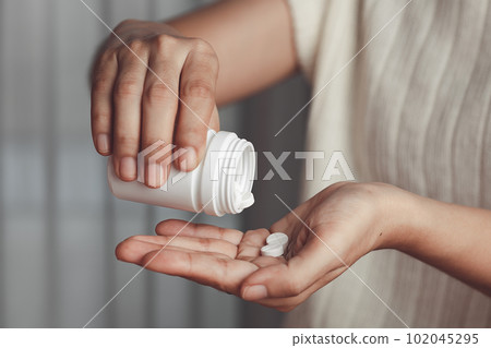Asian woman's hand pouring medicines from a white bottle for medical and healthcare concept. Asian woman's hand pouring medicines from a white bottle for medical and healthcare concept. 102045295