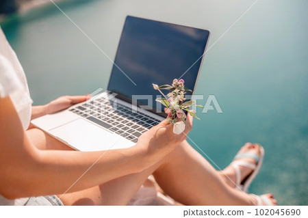 Freelance woman working on a laptop by the sea, typing away on the keyboard while enjoying the beautiful view, highlighting the idea of remote work. Freelance woman working on a laptop by the sea, typing away on the keyboard while enjoying the beautiful view, highlighting the idea of remote work. 102045690
