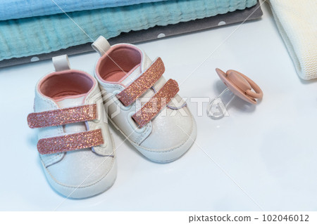 Baby girl pink shoes with other newborn baby accessories on white surface. Baby concept Baby girl pink shoes with other newborn baby accessories on white surface. Baby concept 102046012