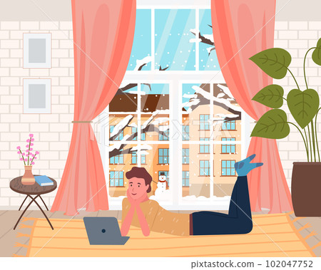 Leisure time at home, man lying on carpet and watching film at laptop, snowy winter outside 102047752