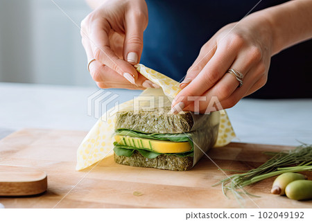 Woman hands wrapping a healthy sandwich in beeswax food wrap. Generative AI 102049192