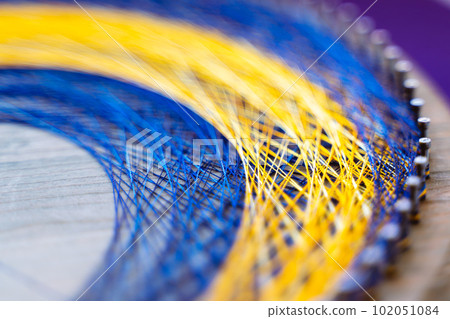 Colored thread mandala on a wooden board with nails. Mandala Moon Harmony Sun esotericism and psychology pictures from yellow and blue silk threads. 102051084