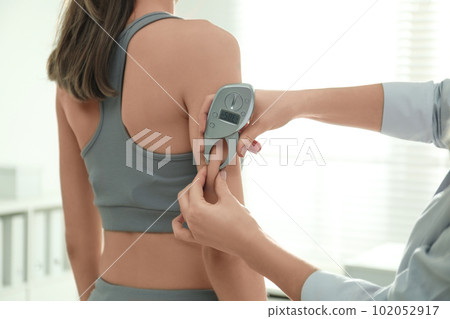 Nutritionist measuring woman's fat layer with caliper indoors, closeup 102052917