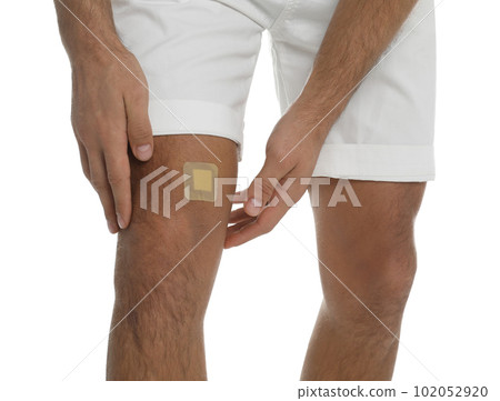 Man with sticking plaster on knee against white background, closeup Man with sticking plaster on knee against white background, closeup 102052920