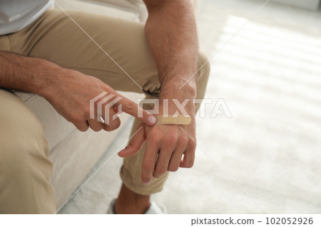 Man putting sticking plaster onto hand indoors, closeup Man putting sticking plaster onto hand indoors, closeup 102052926