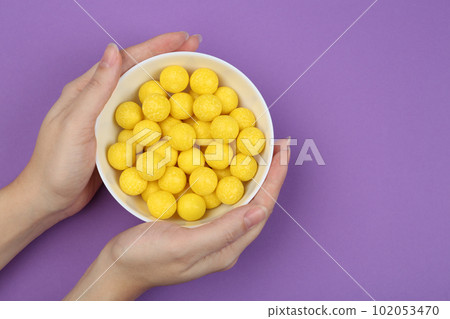 Woman holding bowl of lemon drops on purple background, top view Woman holding bowl of lemon drops on purple background, top view 102053470