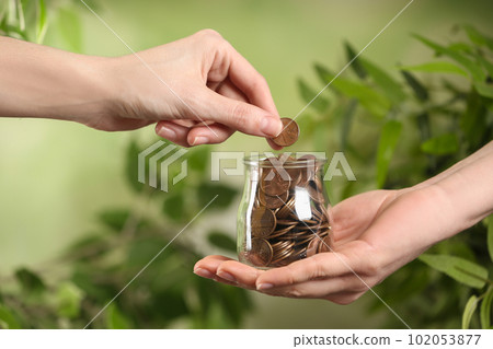 Woman giving coin to other person on blurred background, closeup. Money transfer 102053877