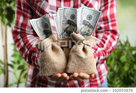 Woman holding sacks with dollars on blurred background, closeup. Money savings Woman holding sacks with dollars on blurred background, closeup. Money savings 102053878