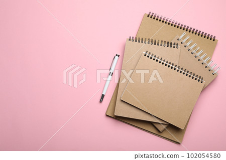 Stylish kraft notebooks and pen on pink background, flat lay. Space for text 102054580