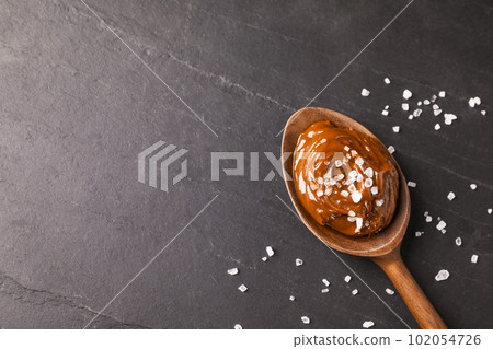 Salted caramel in spoon on grey table, flat lay. Space for text 102054726