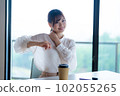 Young female worker stretching and refreshing by the window in the office overlooking greenery 102055265