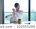 Young female worker stretching and refreshing by the window in the office overlooking greenery 102055266