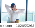 Young female worker stretching and refreshing by the window in the office overlooking greenery 102055268