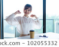 Young female worker stretching and refreshing by the window in the office overlooking greenery 102055332