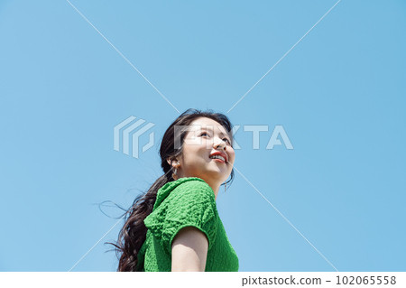 Fashion image of a woman in her twenties smiling and looking up at the blue sky 102065558