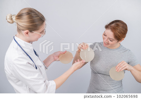 Caucasian woman trying on breast implants. A plastic surgeon helps a patient with a choice. Caucasian woman trying on breast implants. A plastic surgeon helps a patient with a choice. 102065698