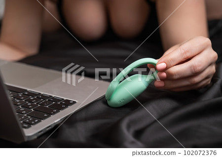 A woman lies on a bed and synchronizes the kegel machine with a laptop. 102072376