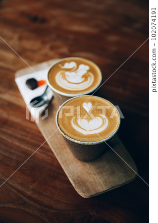 Two cups of cappuccino with latte art on wooden background. Two cups of cappuccino with latte art on wooden background. 102074191