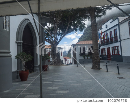 Square with town hall and church Iglesia de San Marcos Evangelista in traditional style. Village of Agulo located in green valley at north coast. Cloudy winter day. La Gomera, Canary Islands, Spain. Square with town hall and church Iglesia de San Marcos Evangelista in traditional style. Village of Agulo located in green valley at north coast. Cloudy winter day. La Gomera, Canary Islands, Spain. 102076758