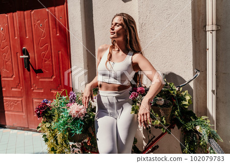 a beautiful girl in a white training suit is going to ride a bike on a sunny summer day. a beautiful girl in a white training suit is going to ride a bike on a sunny summer day. 102079783