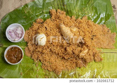 Hot chicken biryani with egg, raita and onion in banana leaf. A popular spicy non-vegetarian dish of India. top view Hot chicken biryani with egg, raita and onion in banana leaf. A popular spicy non-vegetarian dish of India. top view 102081712