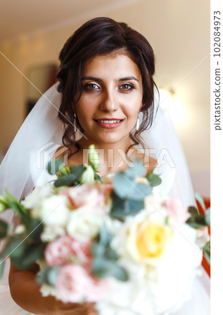 Morning of the bride. Beautiful smiling brunette bride in a white dress with a wedding bouquet in her hands. 102084973
