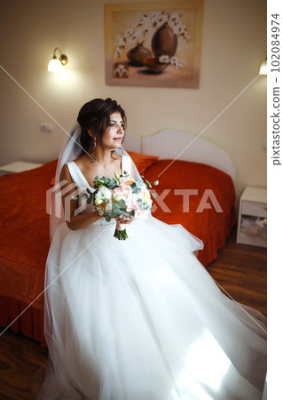 Morning of the bride. Beautiful smiling brunette bride in a white dress with a wedding bouquet in her hands. 102084974