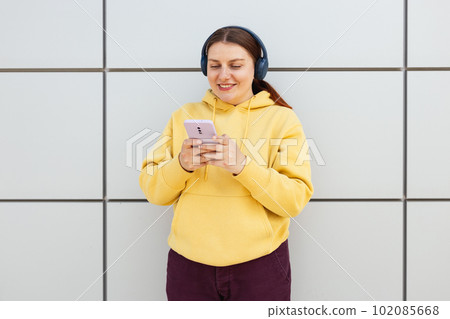 Closeup portrait of a lovely young girl listening to music through wireless earphones and singing on gray background. Music lover enjoying music. Woman record voice by mobie cell phone dictaphone Closeup portrait of a lovely young girl listening to music through wireless earphones and singing on gray background. Music lover enjoying music. Woman record voice by mobie cell phone dictaphone 102085668