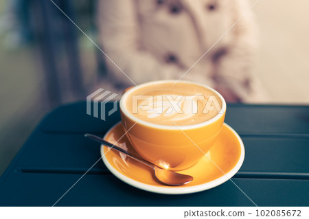 Cup of cappuccino with latte art. Coffee in yellow cup on table in cafe. Enjoy moment, take a break. Cup of cappuccino with latte art. Coffee in yellow cup on table in cafe. Enjoy moment, take a break. 102085672