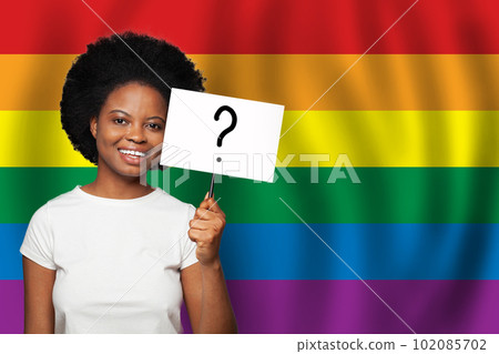 Happy smiling african american woman holding sign with question mark on it on LGBT flag background 102085702