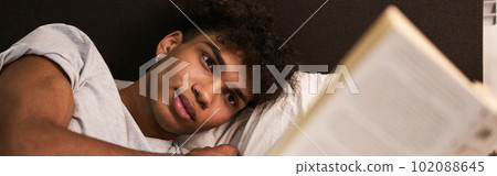 Avoid gadgets before bed. Portrait of calm brunette guy lying in the bed at home, resting and reading interesting book before going to sleep Avoid gadgets before bed. Portrait of calm brunette guy lying in the bed at home, resting and reading interesting book before going to sleep 102088645