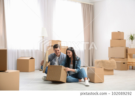 Happy couple unpacking cardboard boxes in their new flat on moving day 102089292