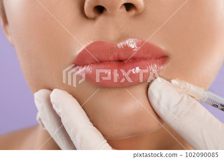 Young woman getting lips injection on lilac background, closeup Young woman getting lips injection on lilac background, closeup 102090085