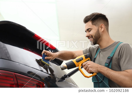 Worker tinting car window with heat gun in workshop 102092186
