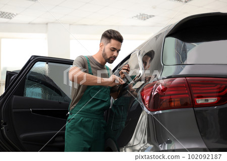 Worker tinting car window with foil in workshop Worker tinting car window with foil in workshop 102092187