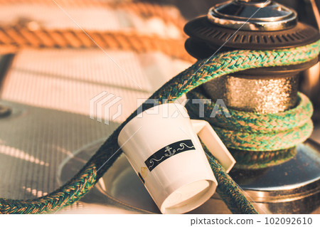 White cup with drawn helm on deck of a white yacht, ship, boat. Concept of tea coffee drinking while traveling at sea ocean. A mug in morning sunlight. Nautical wallpaper. Travel around the world. 102092610