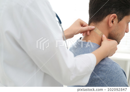 Doctor putting sticking plaster onto man's neck indoors, closeup 102092847