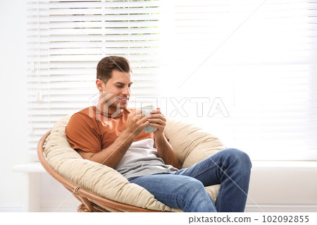 Attractive man relaxing in papasan chair near window at home 102092855