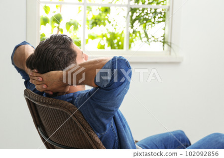 Man relaxing in armchair near window at home Man relaxing in armchair near window at home 102092856