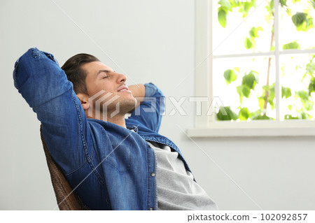 Attractive man relaxing in armchair near window at home Attractive man relaxing in armchair near window at home 102092857