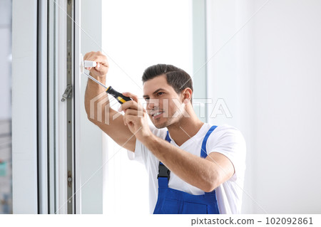 Construction worker repairing plastic window with screwdriver indoors 102092861