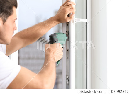 Construction worker repairing plastic window with screwdriver indoors, closeup 102092862