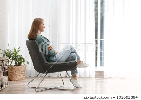 Young woman sitting in armchair near window at home Young woman sitting in armchair near window at home 102092884