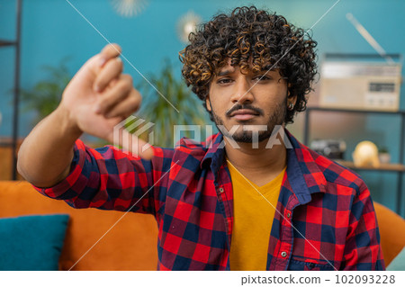 Upset indian man showing thumbs down, dislike bad work, disapproval, dissatisfied feedback at home 102093228